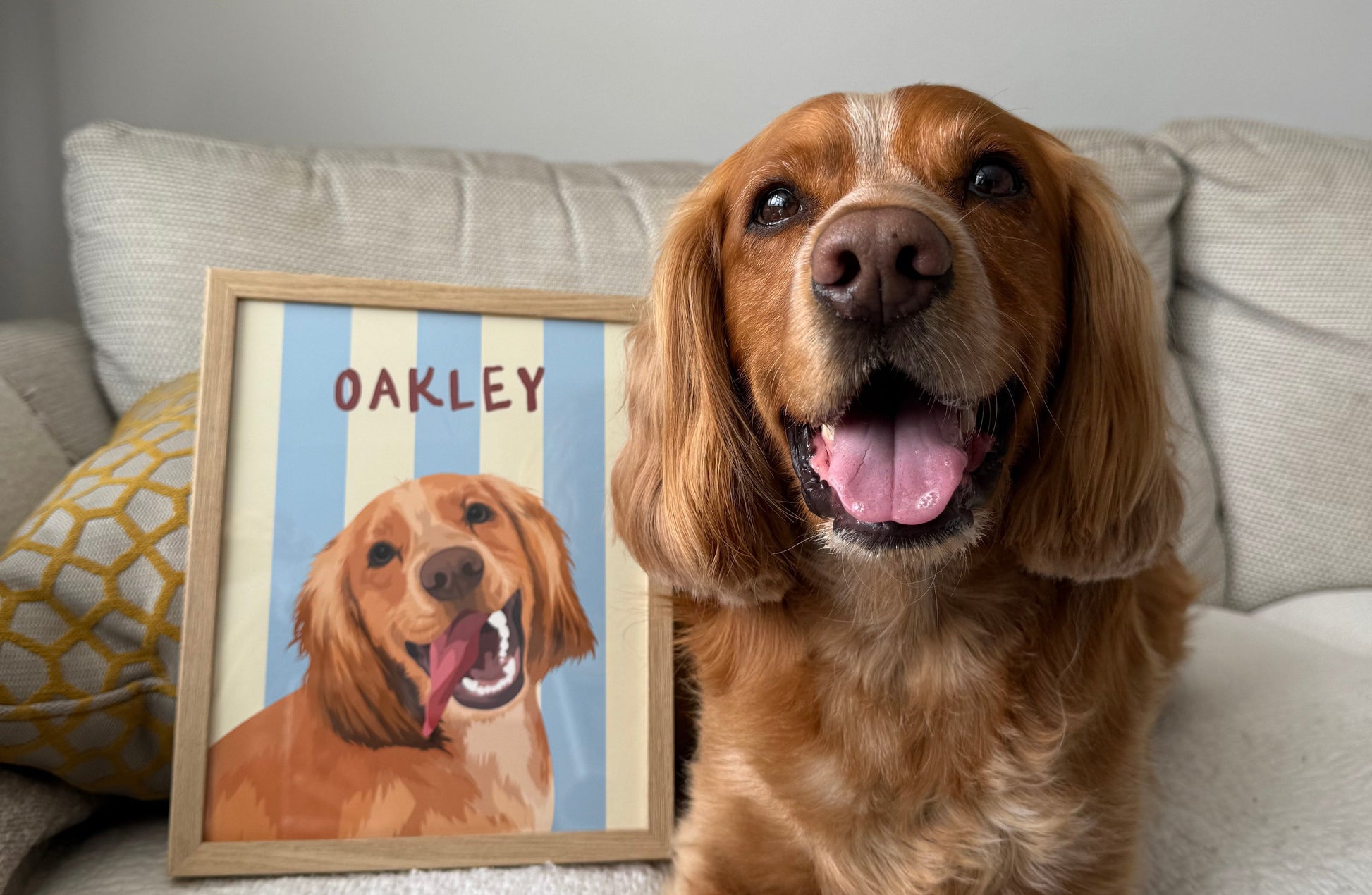 Smiling golden dog named Oakley sitting beside framed custom pet portrait with blue and cream beach stripes background — handmade dog portrait.